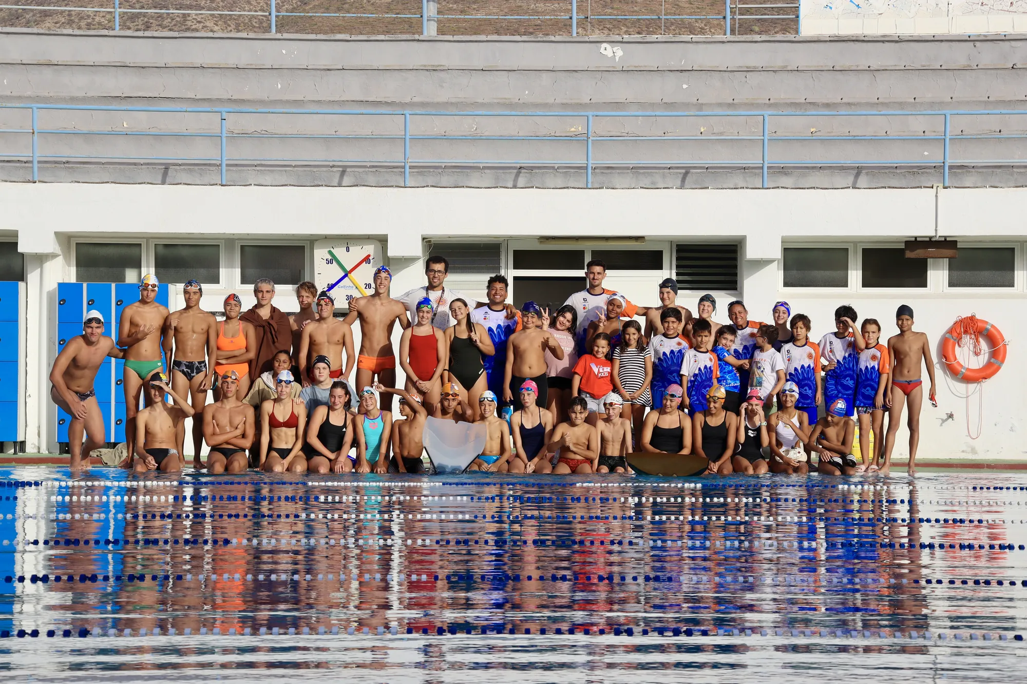 Foto de grupo de nadadores y entrenadores del club al borde de la piscina